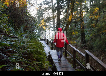 Jeune fille portant un veston rouge est la marche de la magnifique forêt en une matinée d'hiver. Prises à Ucluelet, île de Vancouver, BC, Canada. Banque D'Images