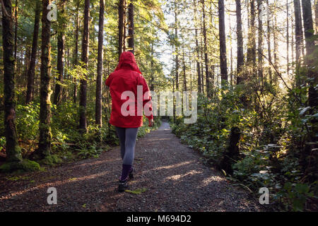 Jeune fille portant un veston rouge est la marche de la magnifique forêt en une matinée d'hiver. Prises à Ucluelet, île de Vancouver, BC, Canada. Banque D'Images