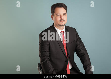 Portrait de l'analyse intérimaire businessman sitting lookking sérieusement à huis clos. Piscine, studio shot, isolé sur fond gris ou bleu clair Banque D'Images