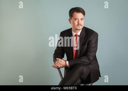 Portrait de l'analyse intérimaire assis handsome businessman. Piscine, studio shot, isolé sur fond gris ou bleu clair Banque D'Images