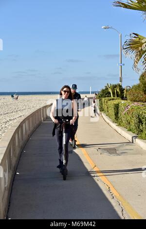 Woman riding sur tous les oiseaux-scooter électrique le long de la plage populaire promenade pavée de Mission Beach, San Diego, California, USA Banque D'Images