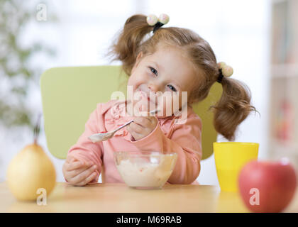 Tout-petit enfant drôle de manger des aliments sains avec une cuillère à la maison Banque D'Images