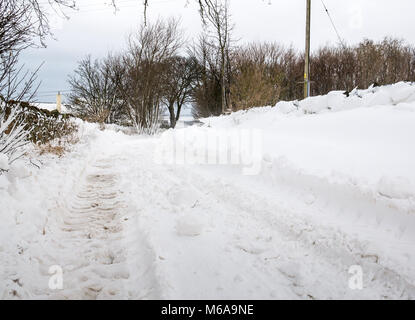 East Lothian, Ecosse, Royaume-Uni, 2 mars 2018. Météo France : la "bête de l'Est arctique' agrippe le paysage rural. Les amoncellements de neige sur certaines sections de la route sont plusieurs pieds de haut dans les lieux, créant un pays des merveilles d'hiver avec scène les traces de pneus du tracteur sur la route couverte de neige Banque D'Images