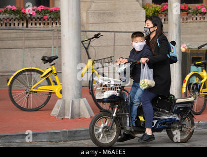 Shanghai, Chine - 18 novembre 2017 : Chinese Woman and boy, portant des masques, monter un vélo motorisé dans les rues de Shanghai. Banque D'Images