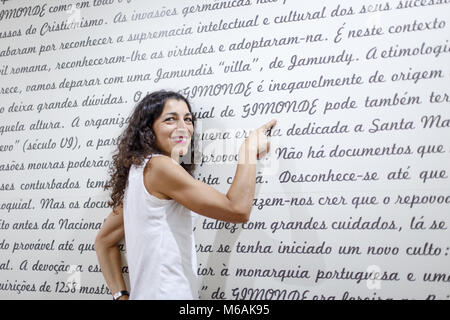 Portrair de belle jeune femme en pointant un doigt sur le mot Gimonde sur un mur avec l'histoire écrite de ce village dans la municipalité de Brag Banque D'Images