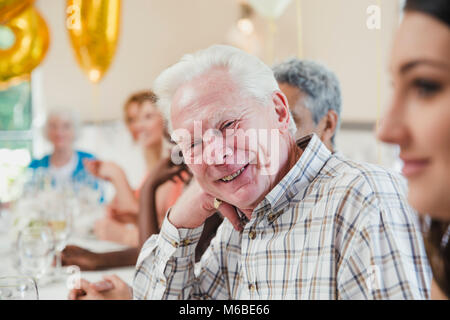 Happy senior man at a Birthday party avec ses amis et sa famille. Il est assis à la table pour la caméra avec sa tête reposant sur sa main. Banque D'Images