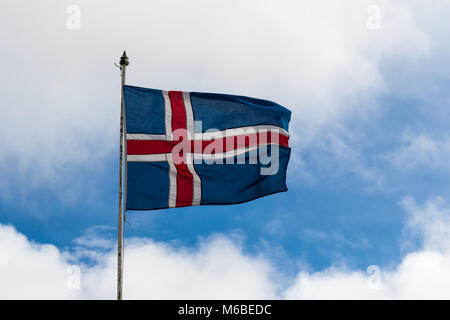 Drapeau islandais soufflé au soleil contre un ciel bleu avec des nuages gris Banque D'Images