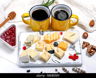 Différents morceaux de fromage sur une planche de bois blanc et jaune deux tasses avec un verre, Close up Banque D'Images