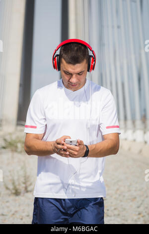 Portrait de l'homme remise en forme runner avec smart phone sms sms et écouter de la musique avec un casque outdoor Banque D'Images