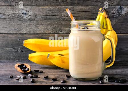 Smoothie banane, café dans un pot Mason avec des grains de café et les bananes en arrière-plan. Vue latérale contre un arrière-plan en bois rustique. Banque D'Images