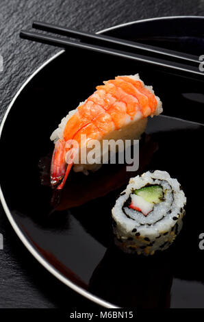 Sushi sur une plaque noire : Nigiri (poisson servi sur du riz) avec du riz (rouleau uramaki sur l'extérieur) et baguettes Banque D'Images