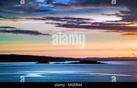 Vue d'un coucher de soleil sur les îles Summer à distance le long de la côte ouest de l'Écosse. Banque D'Images