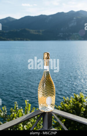 Bien conçu et une bouteille de champagne encore fermé sur une balustrade au lac avec la rive opposée à l'arrière-plan Banque D'Images