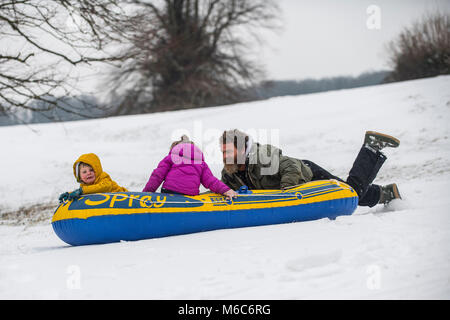 Phil Rogers et enfants Rocco et Ruby bob à l'aide d'un canot pneumatique à Batheaston dans Somerset après de fortes chutes de neige. Bête de l'Est, tempête Emma. Banque D'Images