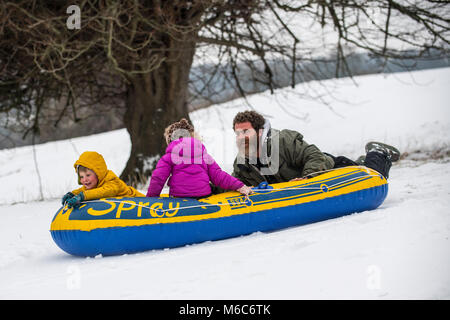 Phil Rogers et enfants Rocco et Ruby bob à l'aide d'un canot pneumatique à Batheaston dans Somerset après de fortes chutes de neige. Bête de l'Est, tempête Emma. Banque D'Images