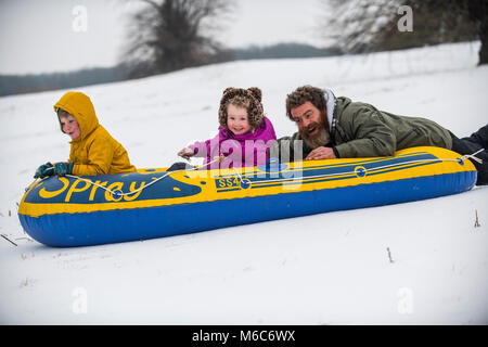 Phil Rogers et enfants Rocco et Ruby bob à l'aide d'un canot pneumatique à Batheaston dans Somerset après de fortes chutes de neige. Bête de l'Est, tempête Emma. Banque D'Images