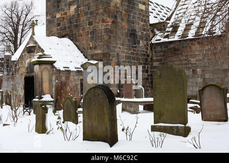 Pierres tombales couvertes de neige et de l'église dans le domaine de l'ancienne église paroissiale à Corstorphine, Édimbourg Banque D'Images