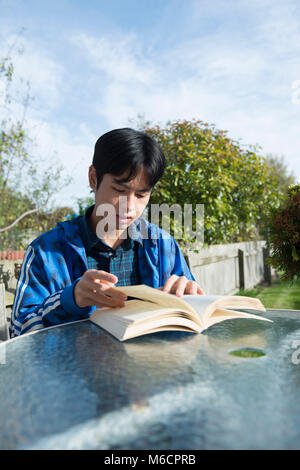 Un jeune étudiant asiatique se trouve à l'extérieur dans le jardin de la chambre d'étudiant la lecture d'un livre Banque D'Images