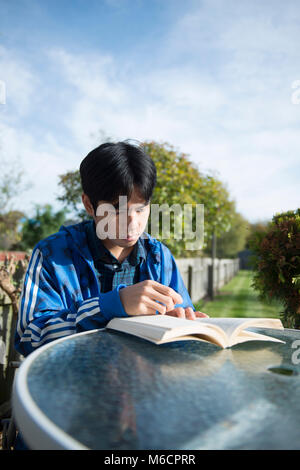 Un jeune étudiant asiatique se trouve à l'extérieur dans le jardin de la chambre d'étudiant la lecture d'un livre Banque D'Images