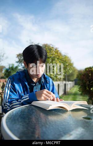 Un jeune étudiant asiatique se trouve à l'extérieur dans le jardin de la chambre d'étudiant la lecture d'un livre Banque D'Images