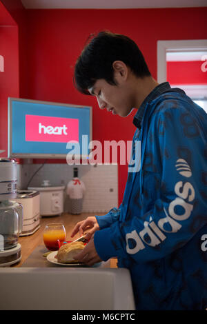 Un jeune étudiant international outre-mer asiatique obtient et prépare son déjeuner dans la cuisine de sa famille d'accueil home Banque D'Images