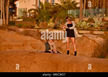 Les femmes d'âge moyen, superbe sur les falaises regardant coucher du soleil doré, contrôle des téléphones cellulaires intelligents pour les messages, au coucher du soleil les falaises, San Diego, Californie, USA. Banque D'Images