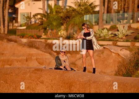 Les femmes d'âge moyen, superbe sur les falaises regardant coucher du soleil doré, contrôle des téléphones cellulaires intelligents pour les messages, au coucher du soleil les falaises, San Diego, Californie, USA. Banque D'Images