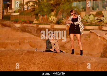 Les femmes d'âge moyen, superbe sur les falaises regardant coucher du soleil doré, contrôle des téléphones cellulaires intelligents pour les messages, au coucher du soleil les falaises, San Diego, Californie, USA. Banque D'Images