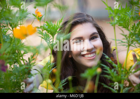 Portrait of a smiling woman with cheveux brun foncé dans un jardin avec des fleurs orange de l'arrière-plan Banque D'Images