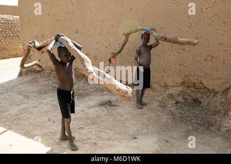 Deux jeunes autochtones, ethniques, les garçons de la tribu Bozo transportant chacun une branche d'un arbre dans leur village. Le Mali, Afrique de l'Ouest. Banque D'Images