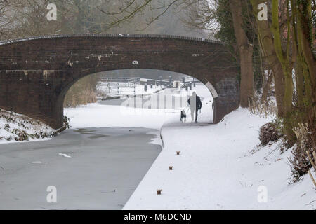 Après le temps froid en mars un homme promène son chien le long du canal de Coventry à Atherstone qui a été gelé et recouvert de neige Crédit : David Warren/Alamy Live News Banque D'Images