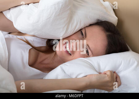 Femme perturbée au lit couvrant des oreilles pour arrêter le bruit Banque D'Images