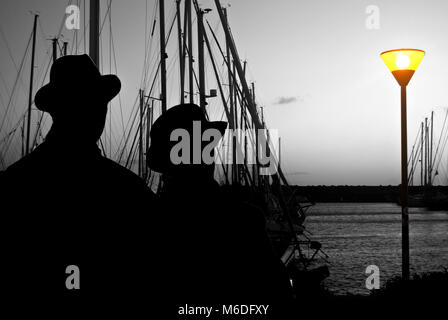 Silhouette de couple des montres amoureux l'horizon au coucher du soleil dans un port Banque D'Images