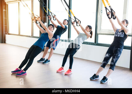 Équipe de formation avec des gens d'Asie total TRX résistance corporelle exercices ensemble au soleil de la salle de sport de classe. Banque D'Images