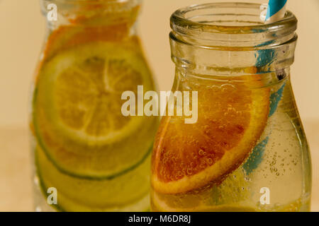 Pour l'eau gazeuse boissons en bouteilles avec de la paille. Tranches d'orange, de citron et de lime. Banque D'Images