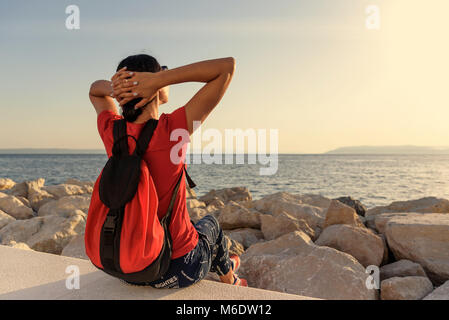 Femme regarde le coucher du soleil, assis sur un pilier de béton. Banque D'Images