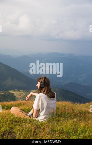 Female hiker en casque avec téléphone cellulaire sur une prairie de montagne des Carpates ukrainiennes Banque D'Images