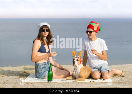 Jeune couple de l'homme et de la femme avec chiot ayant un verre de vin mousseux pour célébrer les vacances de Noël par temps chaud Banque D'Images