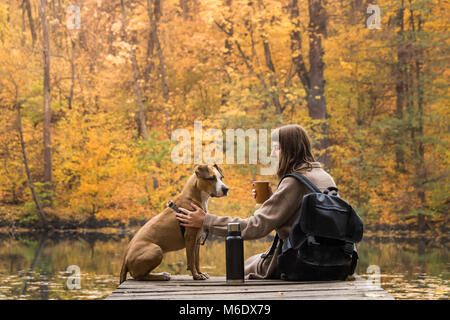 Fille et son animal de compagnie, chien de la randonnée dans la forêt et se reposer à riverbank, femme ayant grand gobelet thermos de café à partir de Banque D'Images