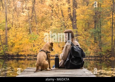 Jeune femme et son chien chiot ayant un repos par le lac sur belle journée d'octobre de l'été indien Banque D'Images