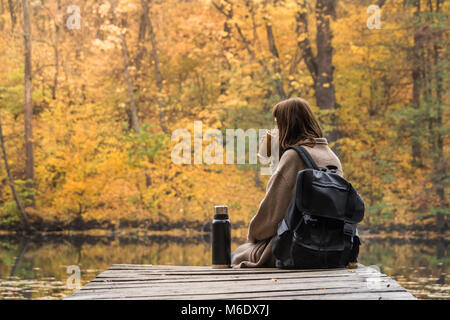 Girl reste et boisson chaude de thermos près du lac dans un parc de la nature sur un jour d'automne d'or Banque D'Images