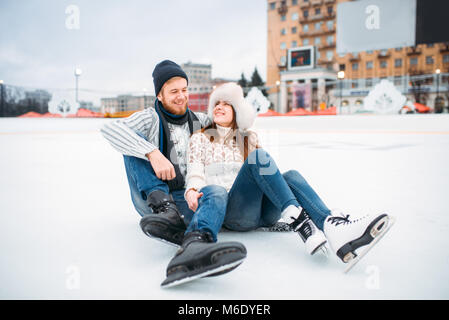 Jeune couple amour assis sur patins à glace, patinoire. Hiver patinage sur open air, des loisirs actifs Banque D'Images