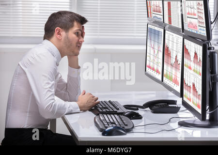 Vue latérale d'un jeune mâle a souligné à l'opérateur à des graphiques sur plusieurs écrans d'ordinateur Banque D'Images