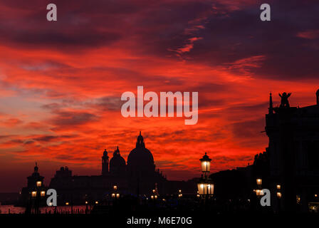 Sang rouge ciel coucher soleil sur la lagune de Venise avec Salute Basilique Saint Marc dômes et lampes de Lion Banque D'Images