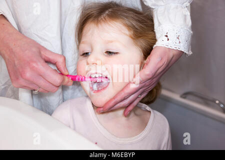 Enfant de trois ans / enfant de 3 ans l'avoir brossé les dents de lait avec une brosse à dents / brosse à dents - par sa mère / mère / maman. Banque D'Images