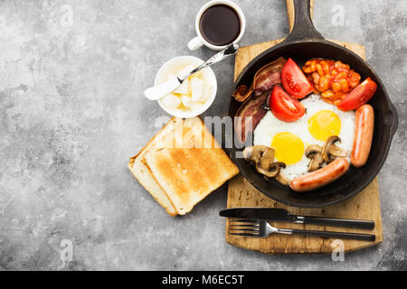 Petit-déjeuner anglais traditionnel - bacon, saucisses, œufs frits, tomates, haricots, champignons, pain grillé avec du beurre - Cuisine à la poêle et du café sur un dos gris Banque D'Images