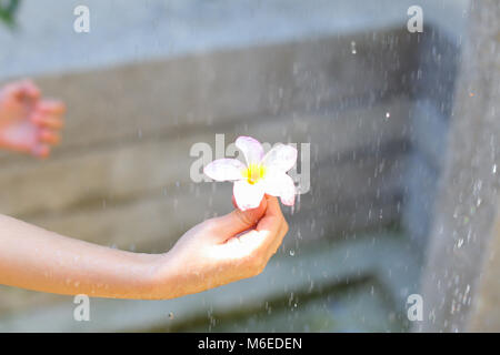 Gouttes d'eau tombent sur l'attente par fleur petite fille aux beaux jours o Banque D'Images