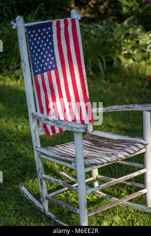 Libre d'un seul blanc rustique peint rocking chair sitting in grass avec le drapeau américain qui pèsent sur l'arrière Banque D'Images