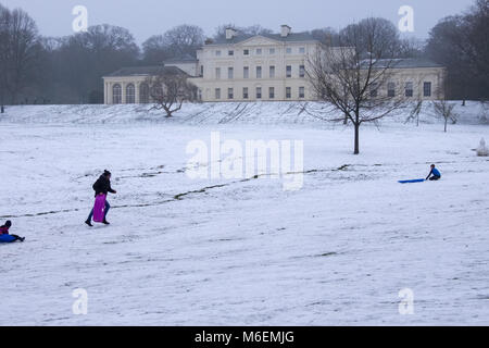 Les adultes et les enfants jouer dans la neige sur Hampstead Heath en face de Kenwood House à Londres après une chute de neige et de froid en hiver 2018. Banque D'Images