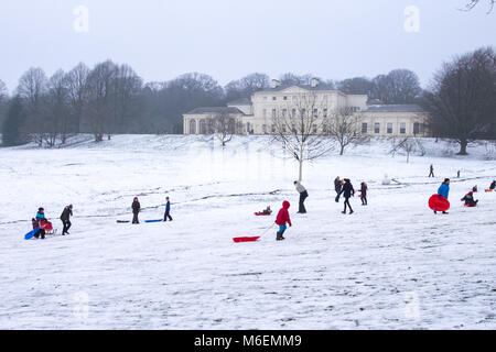 Les adultes et les enfants jouer dans la neige sur Hampstead Heath en face de Kenwood House à Londres après une chute de neige et de froid en hiver 2018. Banque D'Images